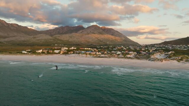 A kitesurfer riding during sunset in front of Pringles Bay town, drone shot.