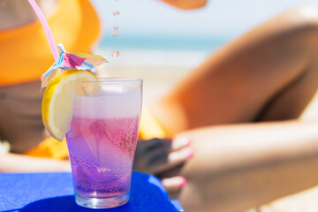 a pink cocktail close-up on the beach, a girl in a swimsuit lies on a sun lounger next to it stands