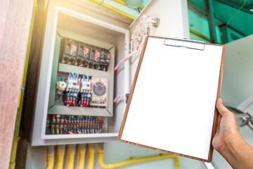 Blank white paper on wooden clipboard in girl hand over blurred electric control box, service and...