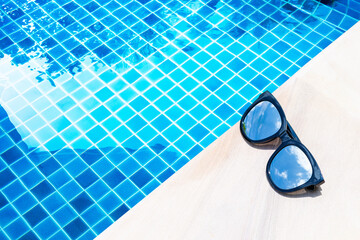 Sunglasses with sky reflection on swimming pool edge with space on blue water background, summer...