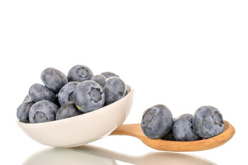 Several sweet blueberries with white saucer and wooden spoon, macro, isolated on white background.