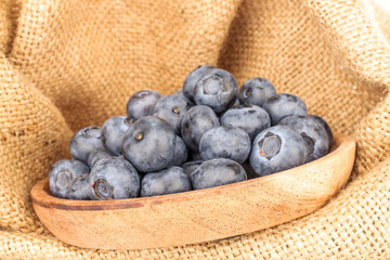 A few sweet blueberries with a wooden saucer on a jute cloth, macro.