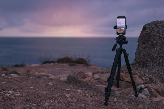 The smartphone camera is on a tripod, photographing a picturesque evening sunset over tropical sea