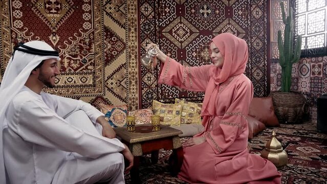 Middle eastern couple spending time together in an arab traditional house . Man with white kandura outfit and woman with colored abaya relaxing at home