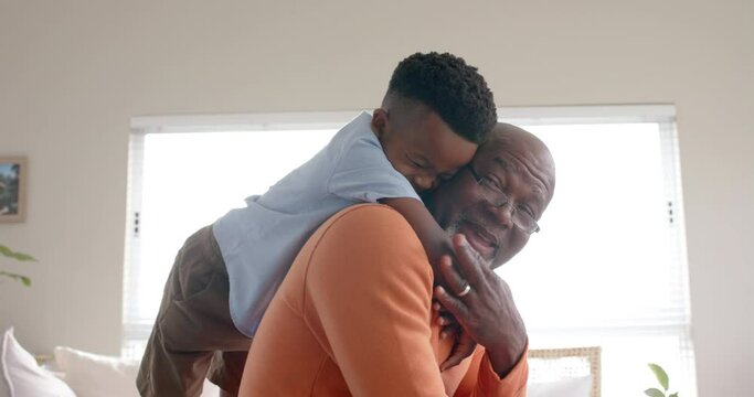 Happy african american grandson and grandfather embracing and smiling on couch at home, slow motion