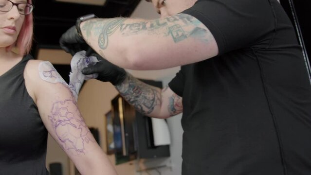 Caucasian Tattoo Artist making a tattoo on a female customer arm