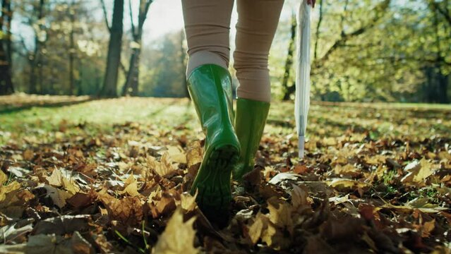 Low section of woman's legs wearing rain boots walking in forest with umbrella. Shot with RED helium camera in 8K.  
