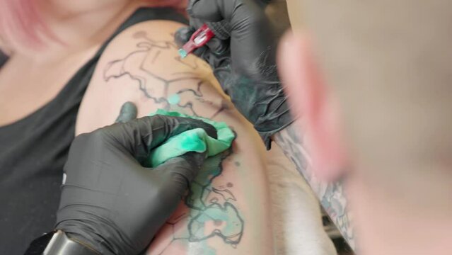 Closeup of a professional Artist making a tattoo on a red hair female arm at a salon