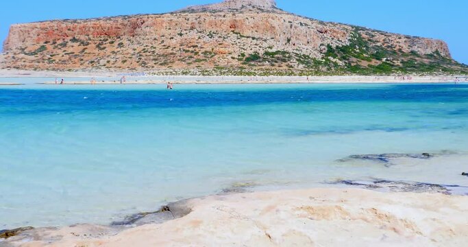 Bathers stroll through beautiful crystal clear waters beach with yellow sand at Balos lagoon on Crete, Greece
