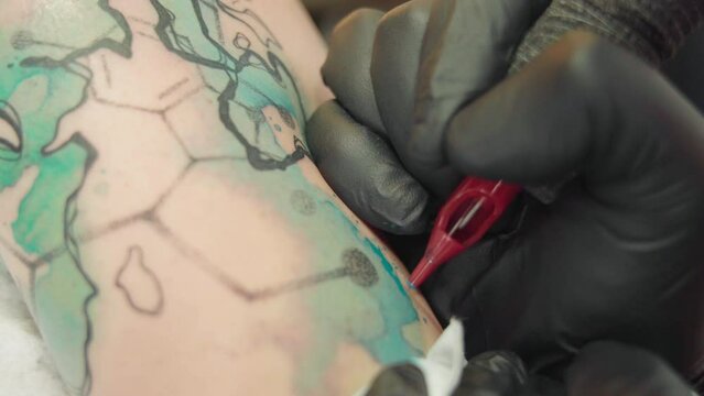 Closeup of an artist man making a tattoo on female arm at a salon