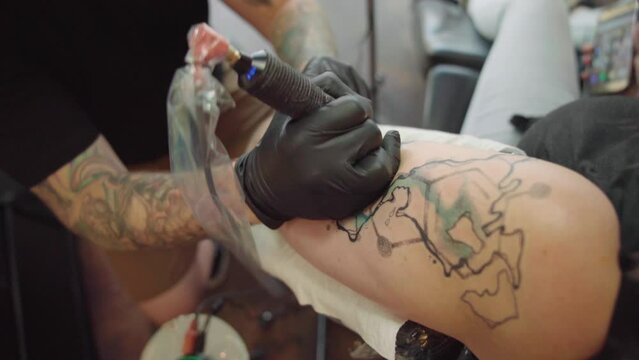 Closeup of an artist man making a tattoo on a female arm at a tattoo salon