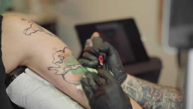 Closeup of an artist man making tattoo with a pen tattoo machine  on a female arm at a tattoo studio