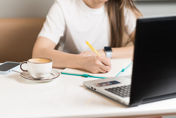 Close-up of the hands of a freelancer girl, writing in a notebook and using a laptop in a cafe. Freelance concept.