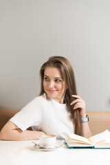 A girl writer is writing a book in a notebook in a cafe.