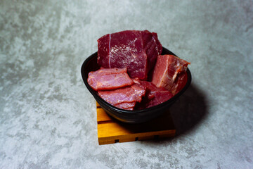 Cuts of fresh beef in a black bowl on a wooden board.  Indulge in the visual allure of meticulously...