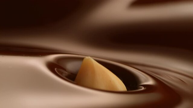 Slow motion of a hazelnuts falling into the brown melted chocolate