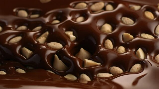 Slow motion of small pieces of hazelnuts falling into the brown melted chocolate