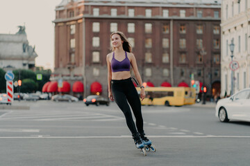 Full length shot of sporty slim woman in active wear rides on blades enjoys outdoor fitness...