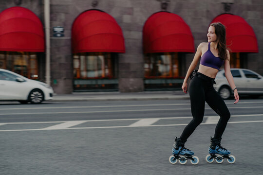 Full length shot of slim active young woman rides rollerblades for strong muscles enjoys favorite hobby has good exercises for figure and health improves muscular endurance increases strength