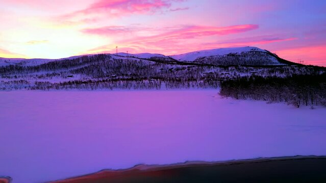 Aerial video of the frozen lake and the rocky mountains covered with snow during pink sunset