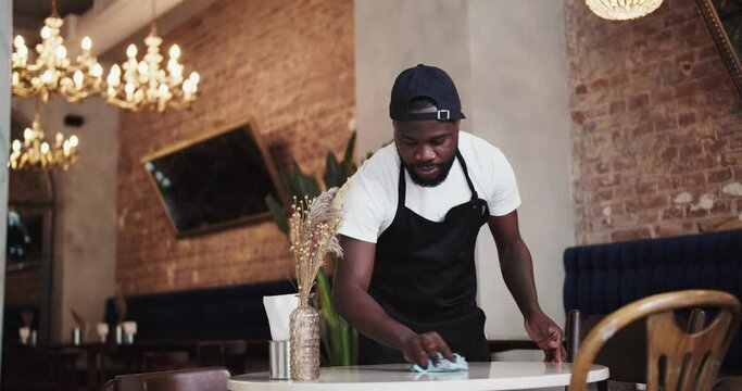 A Black person in a black apron and white T-shirt wipes the table and leaves a Reserved sign. High quality video