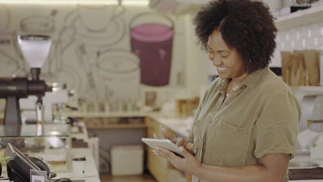 mulher negra Latina atendente em uma cafeteria no Brasil sorrindo usando um tablet para conferir o pedido dos clientes