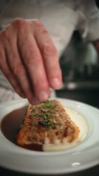 Vertical slow-motion view of a chef sprinkling greens on a lasagna in a sauce