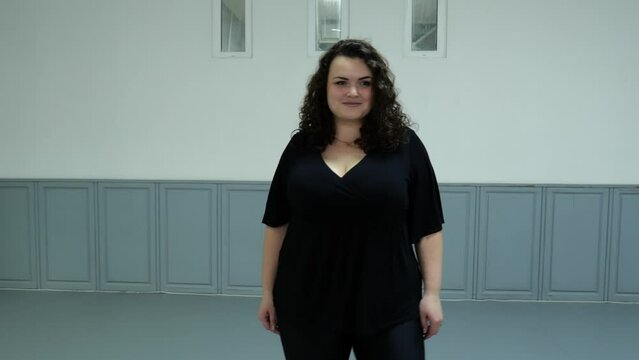Portrait of a plus size model in dark clothes in a dance hall walking forward. Slow motion fat woman