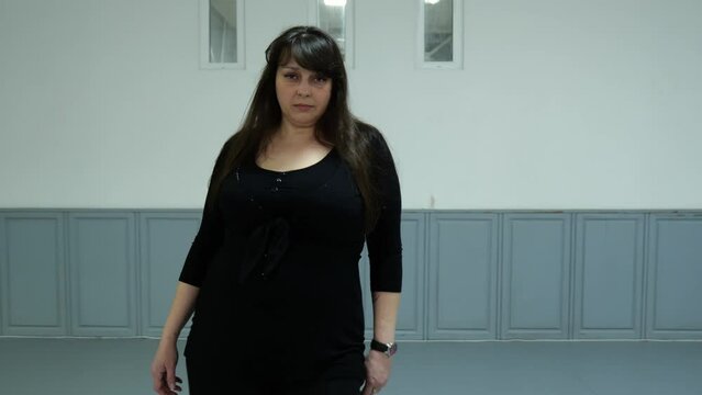 A forty-year-old woman in black clothes dances in the hall. Slow motion dance plus size model. Slow motion portrait woman