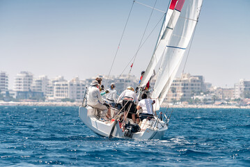 Yacht with crew during regatta in the sea with city on the horizon