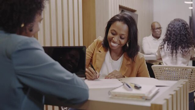 mulher Brasileira cliente de um banco no Brasil sorrindo enquanto assina o contrato de emprestimo bancario e aperta a mao da gerente