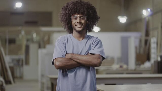 jovem estudante Brasileiro de cabelo black power usando oculos de protecao sorrindo para a camera e cruzando os bracos em uma fabrica no Brasil