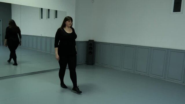 A forty-year-old fat woman in black clothes dances in the hall. Slow motion dance plus size model. Slow dance woman