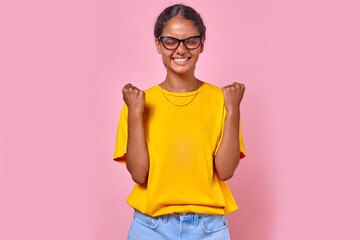 Young overjoyed Indian woman teenager smiles broadly and makes victory gesture with both hands...