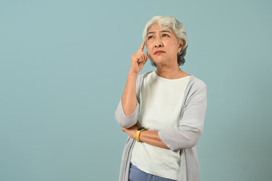 Confused and thoughtful senior woman thinking and looking up expressing doubt and wonder isolated blue background