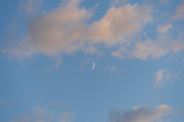 Blue sky with clouds and the moon, the clouds are illuminated by the sun at sunset.