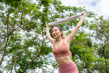 Young attractive Asian woman stretching her arms and legs before her morning exercise run at running track of a local park