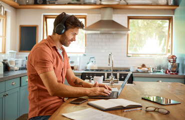 Headphones, home kitchen and man on laptop streaming music, online social media or reading web...