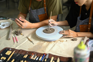 Fototapeta na wymiar Cropped shot of man sculpting clay plate on pottery wheel, creating handmade ceramics in art class