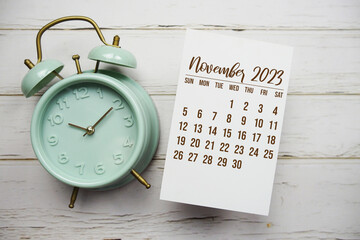 November 2023 monthly calendar and alarm clock on wooden background