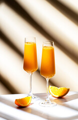 Mimosa summer cocktail drink with orange juice and cold dry champagne or sparkling wine in glasses. Beige background, hard light, shadow pattern
