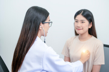 Asian female doctor in uniform holding a stethoscope and using it to measure the heart rate of an asian female patient with heart disease