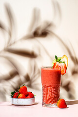 Summer non-alcoholic csmoothie drink with strawberry, banana, syrup, peach juice, lemon and ice in highball glass. Beige pink background, hard light, shadow pattern