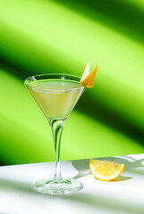 Vesper cocktail drink with dry gin, vodka, aperitif, lemon zest and ice in martini glass. Light green background, hard light, shadow pattern