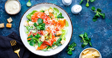 Gourmet Caesar salad with salted salmon, iceberg  lettuce, croutons, parmesan cheese with caesar dressing. Blue stone table background, top view banner