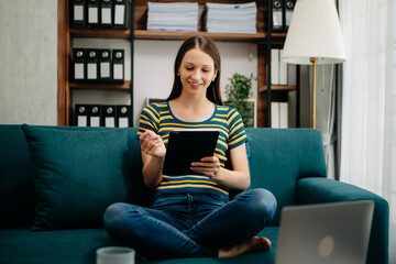 Obraz premium Caucasian woman using the smartphone and tablet on the sofa at home. Embrace Digital Lifestyle