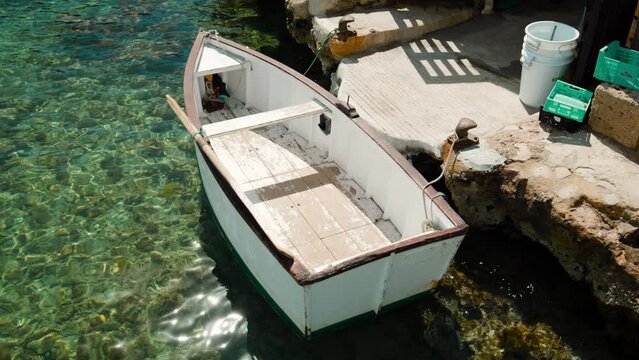Small white rowing boat next to a rustic pier under the sunn