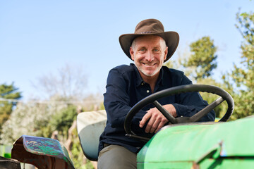 Mature farmer leaning on tractor during sunny day