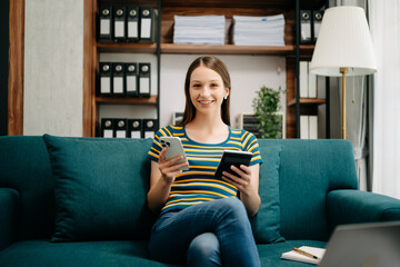 Obraz premium Confident Caucasian woman with a smile standing holding notepad and tablet in living room on the sofa at office