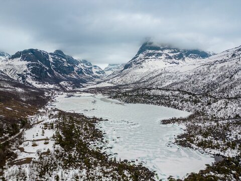 Frozen lake surrounded by snow-capped mountains in a valley on a cloudy day. Trollheimen, Norway.